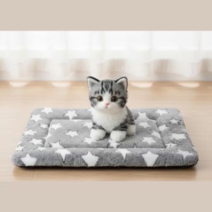 May include: A plush gray and white cat sits on a gray pet bed with white star patterns. The cat has gray and white striped fur and large, round eyes. The pet bed is rectangular.