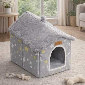 May include: A gray pet house shaped like a house with a star pattern. The house has a fluffy roof and a round opening. A rope toy and a bone-shaped toy are on the carpet in front of the house.