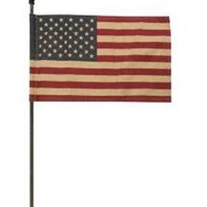 May include: A small American flag with a distressed, vintage appearance. The flag features red and tan stripes and a field of white stars on a dark blue background. The flag is mounted on a dark metal pole.