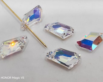 Könnte beinhalten: Fünf klare, rechteckige Kristalle mit schillernden, regenbogenartigen Reflexen. Eine goldfarbene Nadel ist durch einen der Kristalle gesteckt. Die Kristalle sind auf einer hellen Oberfläche angeordnet.