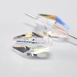 Może przedstawiać: Dwie przezroczyste koraliki szklane o fasetowanym wzorze i iryzującym wykończeniu. Koraliki są nawleczone na cienki drut.