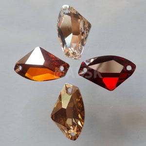 Puede incluir: Cuatro piedras de cristal facetadas en diferentes colores. Las piedras tienen forma de lágrima con un extremo puntiagudo y una base plana. Los colores son transparente, ámbar, rojo y marrón.
