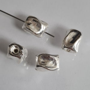 May include: Four silver-colored metal beads with a textured, irregular surface. The beads are irregularly shaped and have a hole in the center for stringing.