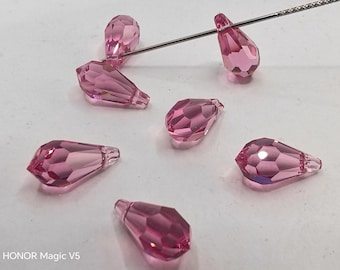 Puede incluir: Cuentas de cristal rosas en forma de lágrima con superficies facetadas. Una aguja plateada atraviesa algunas de las cuentas. Las cuentas están dispuestas sobre una superficie blanca. La imagen destaca la claridad y el color de las cuentas.
