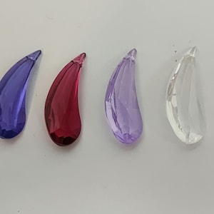 Op de afbeelding: Vier traanvormige kristallen hangers in verschillende kleuren: paars, rood, lichtpaars en helder.