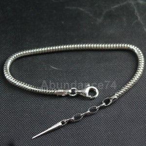 May include: A silver snake chain bracelet with a lobster clasp and a small, sharp, silver pendant.