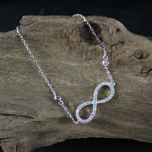 May include: A silver infinity symbol necklace with clear cubic zirconia stones. The necklace is on a silver chain.