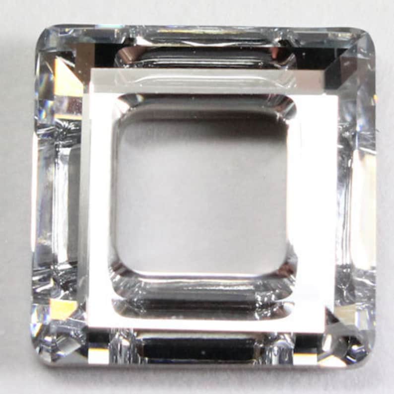 May include: A clear glass square bead with a square hole in the centre. The bead has a faceted design.