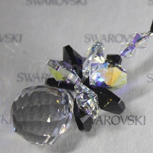 May include: A crystal ornament featuring a clear crystal sphere with a black starburst design. The starburst is made of smaller crystals with iridescent rainbow colours.