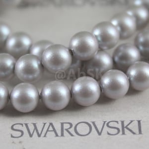 May include: A strand of iridescent gray pearl beads, with the word "SWAROVSKI" printed on the surface below.