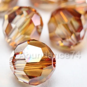 Puede incluir: Primer plano de un grupo de cuentas de vidrio facetadas de color ámbar. Las cuentas son redondas y tienen un acabado brillante e iridiscente.