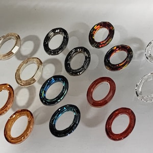 May include: Assortment of oval-shaped glass rings in various colors, including clear, brown, red, blue, and black. The rings are approximately 1 inch in diameter.