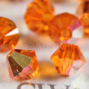 Puede incluir: Primer plano de cuentas de cristal naranja con un diseño facetado. Las cuentas tienen un ligero brillo iridiscente.