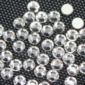 May include: A close-up view of a large quantity of clear rhinestones, arranged in a pattern on a black fabric background.
