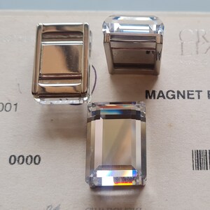 May include: Three clear glass rectangular prism shapes with beveled edges. The prisms are on a white surface with black text that reads "0000" and "MAGNET F".