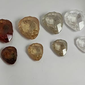 May include: A collection of faceted gemstone pendants in shades of brown, yellow, and clear. The teardrop-shaped pendants have a hole at the top for threading. Suitable for jewellery making, these would be ideal for necklaces.