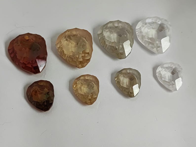 May include: A collection of faceted gemstone pendants in shades of brown, yellow, and clear. The teardrop-shaped pendants have a hole at the top for threading. Suitable for jewellery making, these would be ideal for necklaces.