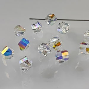 Peut inclure: Un groupe de perles de verre transparentes et irisées, avec un effet arc-en-ciel, éparpillées sur une surface blanche.