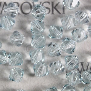 Op de afbeelding: Een close-up van een groep lichtblauwe kristallen kralen. De kralen zijn gefacetteerd en hebben een ronde vorm. Ze zijn willekeurig gerangschikt op een wit oppervlak.