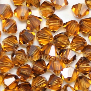 May include: A close-up of a pile of amber-colored glass beads. The beads are faceted and have a shiny finish. They are perfect for jewelry making or other craft projects.