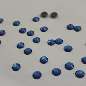 Pode incluir: Uma dispersão de strass azuis iridescentes sobre uma superfície branca.