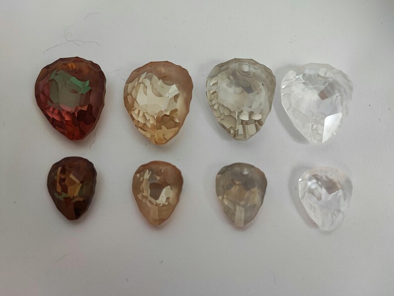 May include: Eight faceted teardrop-shaped gemstones in shades of brown, amber, and clear. The gemstones are arranged in two rows of four, with the top row featuring larger stones. The stones have a polished, reflective surface.