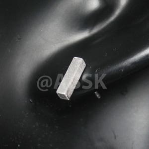 May include: A silver metal key, shaped like a rectangular prism, is lying on a black surface.