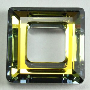 Puede incluir: Una cuenta de vidrio de forma cuadrada, facetada, con un marco interior de color dorado. La cuenta es de color verde oscuro con un ligero tono azul.