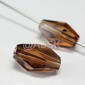 May include: Two brown faceted glass beads with a hole through the center. The beads are on a white surface.