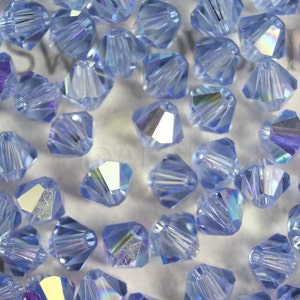 Peut inclure: Gros plan sur un groupe de perles en cristal bleu clair avec un design facett&eacute;. Les perles sont dispos&eacute;es de mani&egrave;re al&eacute;atoire sur une surface blanche.