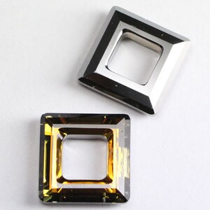 May include: Two square-shaped, open-frame, crystal embellishments. One is silver and the other is amber.