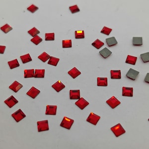 May include: A scattering of red square rhinestones on a white background.