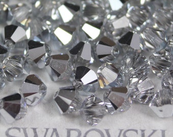 Puede incluir: Primer plano de un montón de cuentas de cristal de color plateado. Las cuentas son facetadas y tienen una superficie reflectante. Las cuentas están etiquetadas con "SWAROVSKI".