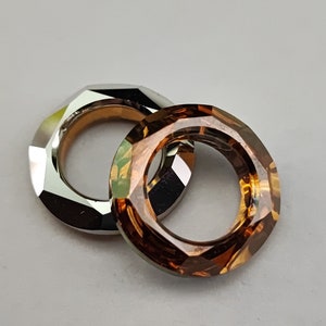 Puede incluir: Dos anillos facetados, uno plateado y otro marrón, están entrelazados. Los anillos son ambos octogonales.