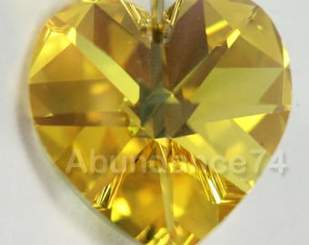 May include: A yellow heart-shaped crystal with a faceted design. The crystal has a hole at the top for hanging.