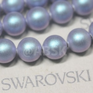May include: A strand of iridescent blue and purple glass beads. The beads are round and have a smooth, polished finish. The beads are strung on a clear thread and are arranged in a random pattern. The beads are all the same size and are about 10mm in diameter. The beads are made by Swarovski.