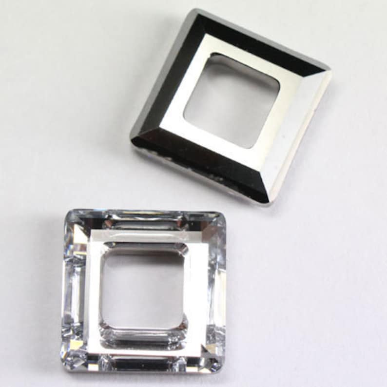 May include: Two silver-toned metal square-shaped frames with a square opening in the centre. The frames are different sizes. The larger frame is slightly raised and has a more polished finish. The smaller frame is flat and has a more matte finish.