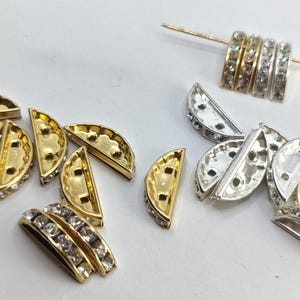 Puede incluir: Un surtido de hallazgos de joyería decorativos, que incluyen cuentas doradas y plateadas en forma de semicírculo con pedrería transparente. También, varias cuentas de anillo doradas y plateadas con pedrería se muestran en un alfiler dorado.