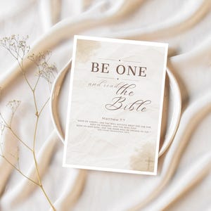 Könnte beinhalten: Ein rechteckiger Druck mit den Worten "BE ONE and read the Bible" in braunem Text. Der Druck befindet sich auf einem weißen Hintergrund mit einem aquarellartigen Design. Der Druck befindet sich auf einem weißen Teller, mit einem Zweig getrockneter Blumen links.