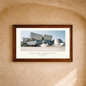 May include: A framed print featuring the Walt Disney Concert Hall in Los Angeles, designed by Frank Gehry in 2003. The image displays the building's metallic, curved, and angular architectural panels against a clear blue sky, with text below.