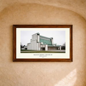 May include: A framed architectural print of Bagsværd Church by Jørn Utzon, 1976. The image features a white and green building with a stepped roofline and geometric facade, set within a dark wood frame against a textured beige wall background.