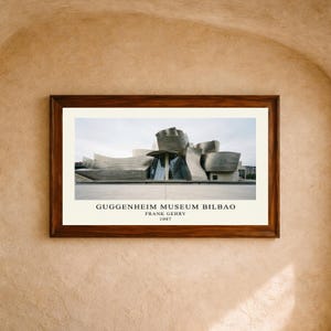 May include: A framed horizontal print featuring the Guggenheim Museum Bilbao, a metallic structure with curved, flowing forms. Below the image, the text reads: GUGGENHEIM MUSEUM BILBAO, FRANK GEHRY, 1997. The print is set within a dark brown wooden frame.