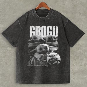 May include: Dark gray t-shirt featuring a black and white graphic of Grogu from The Mandalorian. The word "GROGU" is printed in white block letters above the image. The phrase "I would like to see the baby" is printed below the image.