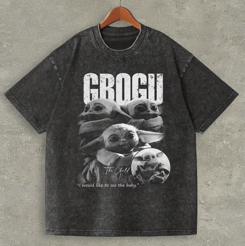May include: Dark gray t-shirt featuring a black and white graphic of Grogu from The Mandalorian. The word "GROGU" is printed in white block letters above the image. The phrase "I would like to see the baby" is printed below the image.
