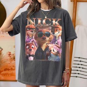 May include: Dark gray t-shirt featuring a graphic of Nick Wilde from Zootopia. The design includes multiple images of the character with sunglasses and the name "Nick Wilde" in a vintage style.