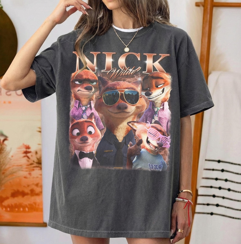 May include: Dark gray t-shirt featuring a graphic of Nick Wilde from Zootopia. The design includes multiple images of the character with sunglasses and the name "Nick Wilde" in a vintage style.