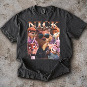 May include: Dark gray t-shirt featuring a graphic of several cartoon foxes, with the text "NICK Wilde" in a gold font. The foxes are wearing sunglasses and formal attire. The shirt is made of a soft material.