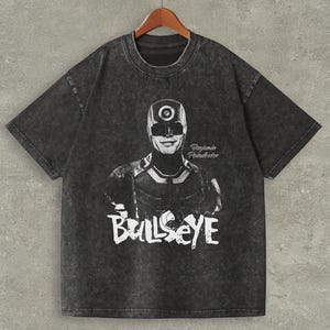 May include: Dark grey t-shirt with a black and white graphic of a character with a target on their head and the word "Bullseye" in white. The name "Benjamin Poindexter" is also printed on the shirt.