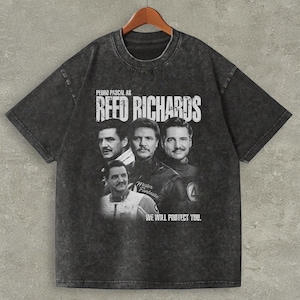 May include: Dark gray t-shirt featuring a graphic of Pedro Pascal as Reed Richards. The design includes multiple images of the actor and the text "REED RICHARDS" and "WE WILL PROTECT YOU."