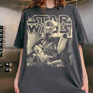 Peut inclure: Un t-shirt gris anthracite &agrave; manches courtes avec une impression graphique vieillie de couleur cr&egrave;me repr&eacute;sentant un clone trooper Star Wars tenant un fusil blaster. Le texte STAR WARS est imprim&eacute; en gras au-dessus du personnage casqu&eacute;.